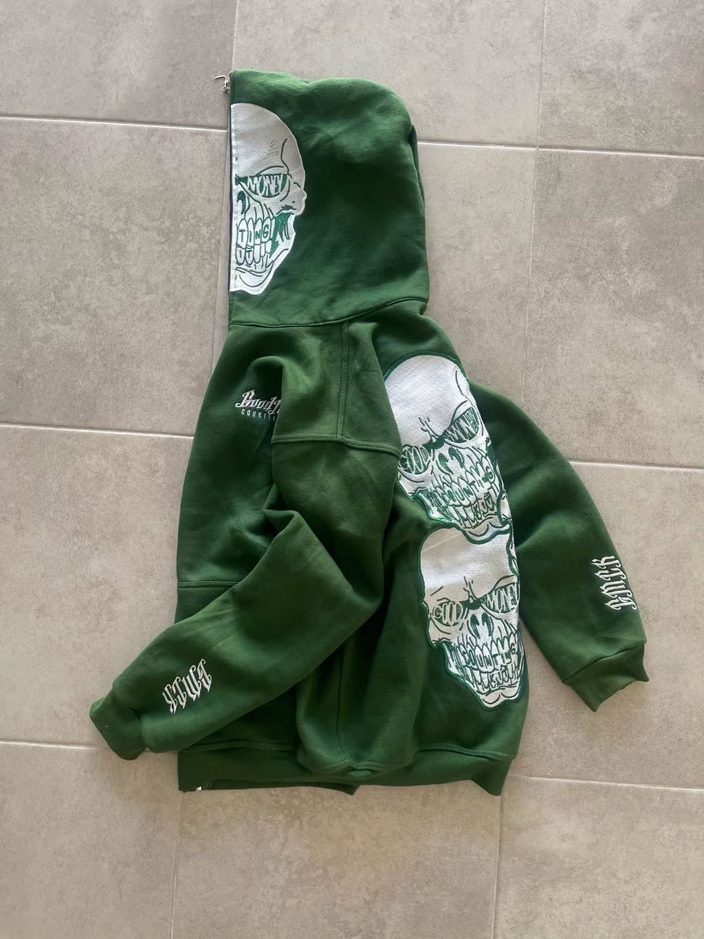 forest green full-zip hoodie (a "full-face zip" style) loaded with heavy, edgy Y2K/streetwear graphics and bold skull motifs