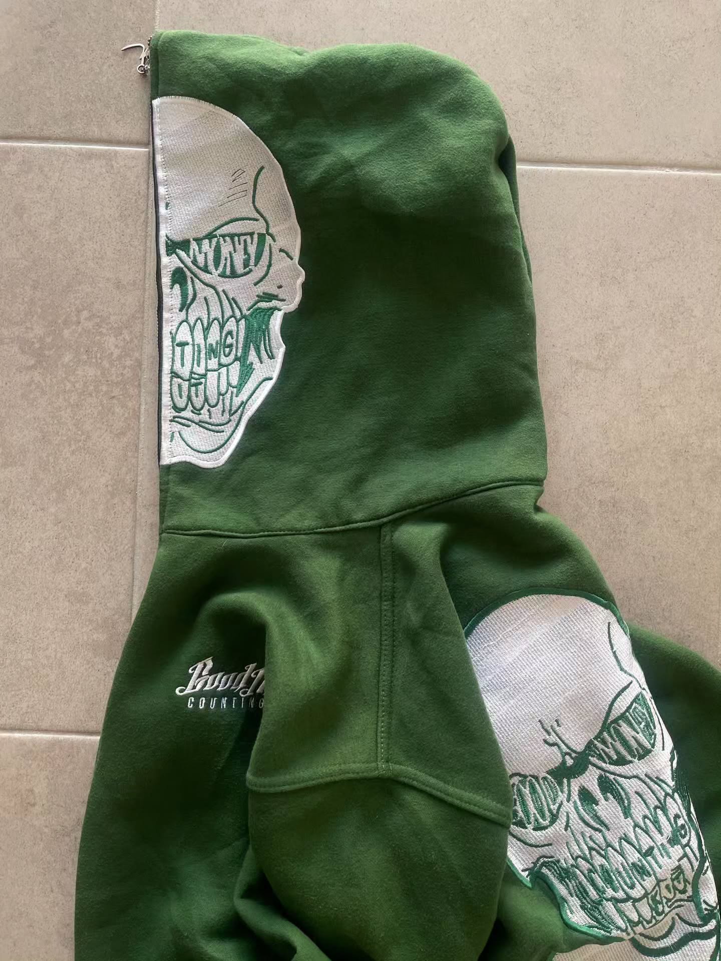 forest green full-zip hoodie (a "full-face zip" style) loaded with heavy, edgy Y2K/streetwear graphics and bold skull motifs