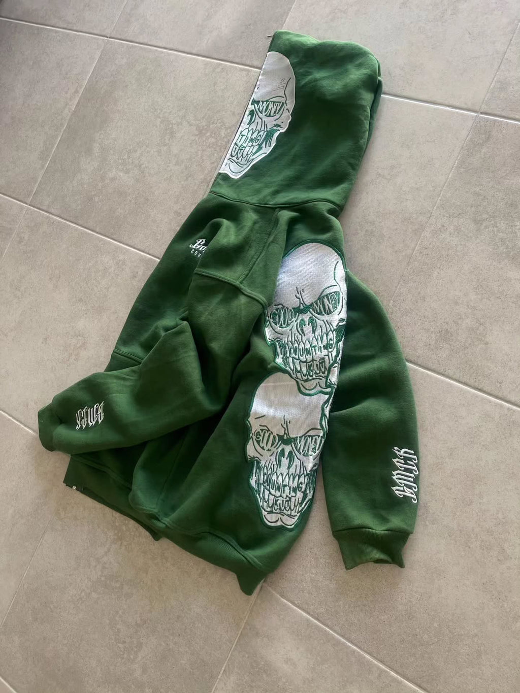 forest green full-zip hoodie (a "full-face zip" style) loaded with heavy, edgy Y2K/streetwear graphics and bold skull motifs