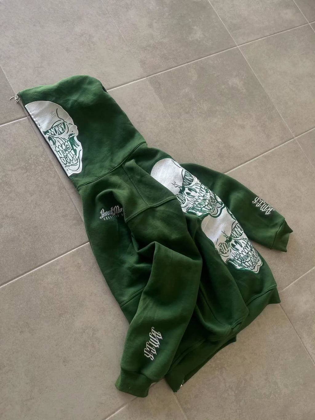 forest green full-zip hoodie (a "full-face zip" style) loaded with heavy, edgy Y2K/streetwear graphics and bold skull motifs