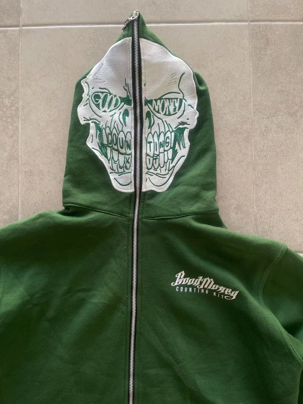 forest green full-zip hoodie (a "full-face zip" style) loaded with heavy, edgy Y2K/streetwear graphics and bold skull motifs